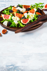 Salad with figs, feta cheese and blackberries in a wooden plate on white background.