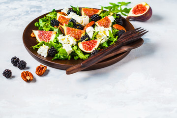 Salad with figs, feta cheese and blackberries in a wooden plate on white background.