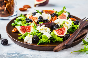 Salad with figs, feta cheese and blackberries in a wooden plate on white background.