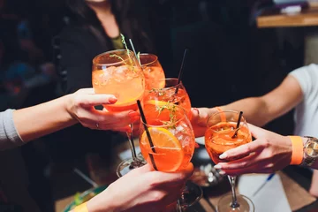 Foto op Plexiglas women raising a glasses of aperol spritz at the dinner table. © Евгений Вершинин