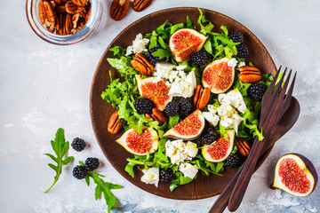 Salad with figs, feta cheese and blackberries in a wooden plate on white background, top view.
