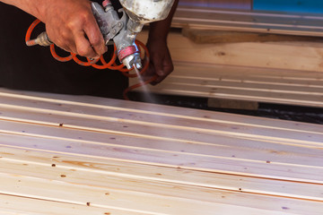 A man covers wooden boards with varnish in the workshop with a spray.