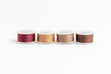 Different spools of brown thread prepared for sewing machine, isolated on white, side view