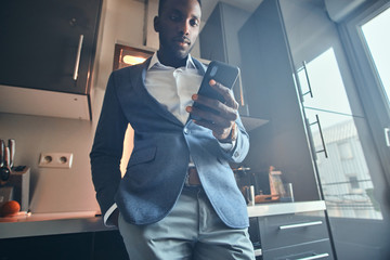 Young african man in white shirt is chatting by mobile phone at the kitchen.