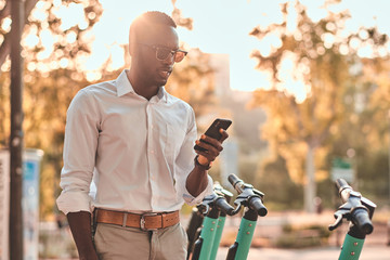 Young african guy is paying for electrical scooter by web payment using his mobile phone.
