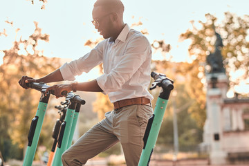 Cheerful smiling man is choosing right scooter from parking at bright sunny day.