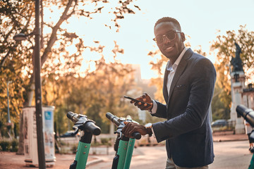 Attractive american tourist in sunglasses is paying for electrical scooter using his mobile phone.