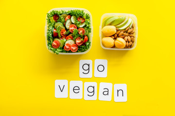 Lunch box with salad and go vegan text on yellow background top view