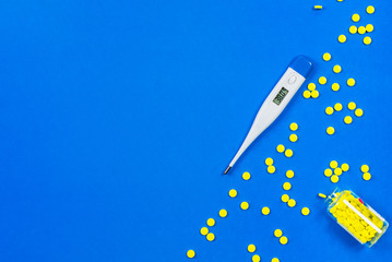 Electronic thermometer with high temperature and yellow pills and a bottle on a blue background. Copy space for text.