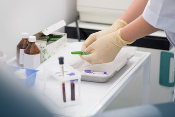 gloved laboratory assistant preparing for blood sampling against a background of blood tubes