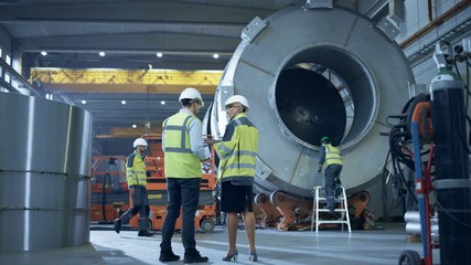 Two Heavy Industry Engineers Stand in Pipe Manufacturing Factory, Use Digital Tablet Computer, Have Discussion