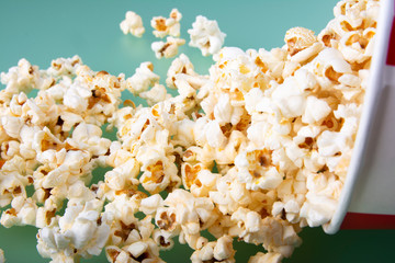 Close-up of box with popcorn spilled on green background. Concept of tasty snacs