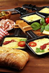 Delicious traditional Swiss melted raclette cheese on diced boiled or baked potato and baguette served in individual skillets with salami..