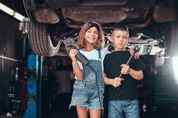 Smiling girl and pensive boy are posing for photographer at auto service workshop.