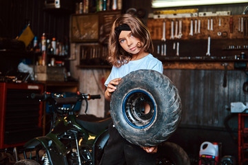 Obraz na płótnie Canvas Nice small girl is posing for photographer with big wheel from car at auto service.