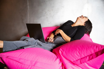Woman laughing with laptop computer  while sitting on pink beanbag chair