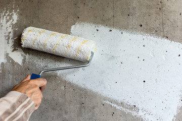 A painter paints a concrete wall with white paint, a male hand with a paint roller for painting a...