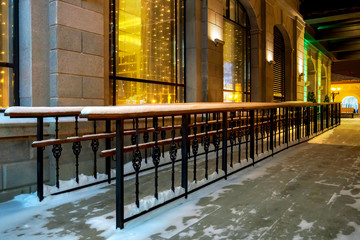 Metal ramp with wooden handrails for wheelchairs and prams along building in winter evening