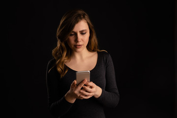 Fototapeta premium Serious woman with phone in her hand looking on it and texting with unhappy face