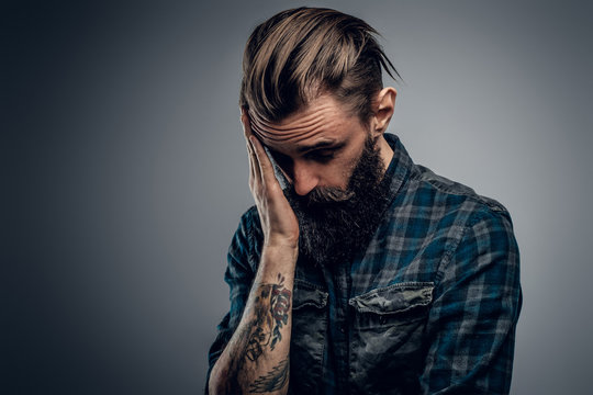 Bearded skinny man with tattooes feels dispair and sorrow while thinking about life.