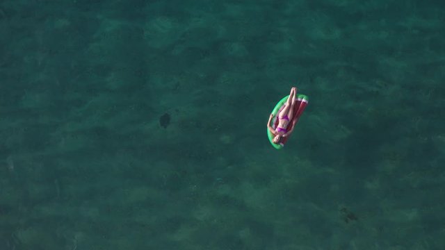 Straight down drone view of slim woman in bikini lying on air lilo ball in turquiose water of Mediterranean sea. Aerial shot of tiny female figure on inflatable watermelon slice in deep blue ocean