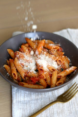 Sprinkling parmesan cheese on a plate of pasta with tomato sauce and eggplant. Selective focus.