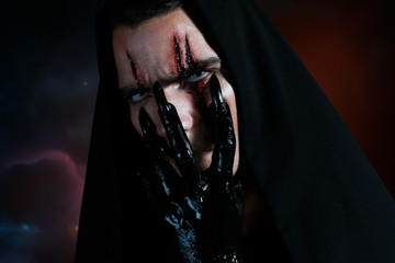 An evil demon hides his face behind his black hand and looking to the camera. Halloween makeup...