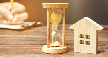 Wooden house and clock. A person signs documents. Signing a contract to rent a house or apartment. Making a will. Testament property. Buying or selling real estate. Mortgage agreement. Leasing