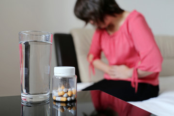 Stomach ache, bottle of pills and water glass on background of woman suffering from abdominal pain....