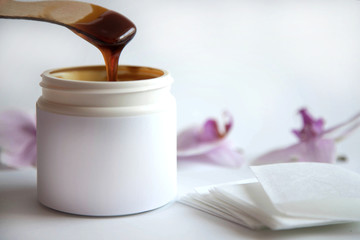 The concept of depilation and beauty is sugar paste or hair removal wax in a white plastic jar with a wooden wax spatula in melted paste and stripes for hair removal next to it.