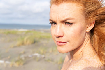 Beautiful woman with red hair and freckles at beach