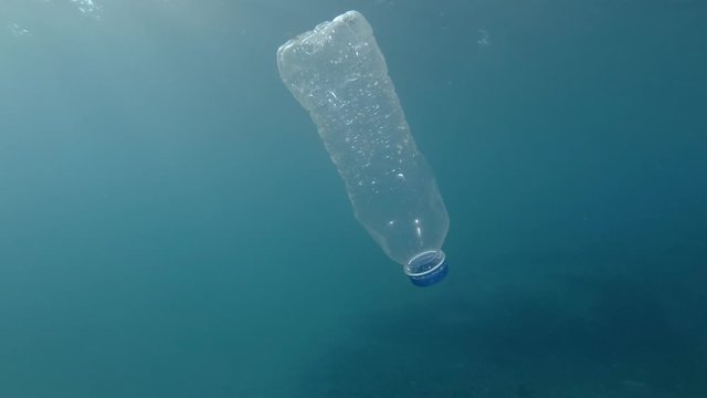  Plastic pollution, plastic bottle in blue water. Discarded plastic bottle slowly drifting under surface of blue water in sunlight. Plastic bottle floats in Mediterranean Sea, Europe. 