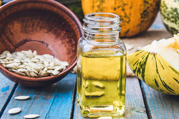 Pumpkin seeds and essential oil in a bottle near the pumpkin on blue old boards.