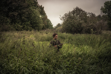Fototapeta na wymiar Hunting hunter boy with gun hiding in tall grass during hunting season