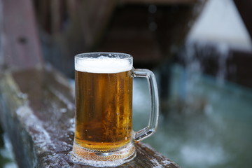 Close-up. Glass of beer with beer foam on a natural wooden board on a background of blue water. Banner, pattern, background.