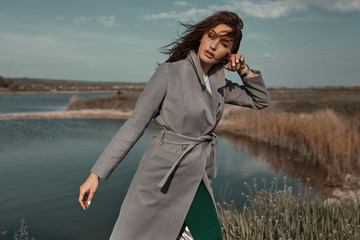 Beautiful elegant portrait of young woman in fashion grey coat outside. Sunny autumn ar spring weather.