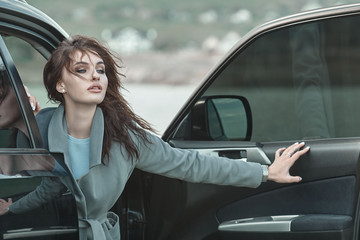 Glamour beautiful woman in trendy coat looking uot of the luxury car.