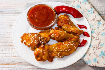 Fried juicy chicken wings marinated with honey, soy sauce, spices, sprinkled with sesame seeds on a white plate with sauce. Asian recipe, top view, close up