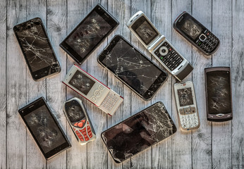 Group of eleven mobile phones of different times, all broken and shattered and of different sizes, placed on a wooden surface
