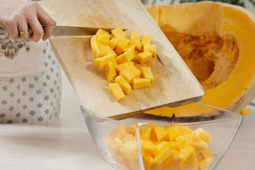 Nóż kuchenny, skóra dyni i pestki dyni leżą na drewnianej desce do krojenia. W tle wielka dynia przekrojona na połowę.