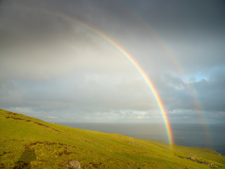 Fototapeta premium rainbows in the sky with clouds above green hill with sea view