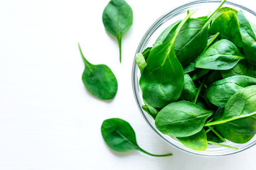 Fresh green spinach leaves in glass bowl on white table. Organic food, healthy diet, vegetarian food. Top view.