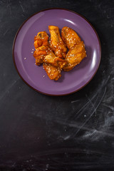 Fried juicy chicken wings marinated with honey, soy sauce, spices, sprinkled with sesame seeds on a plate on a black background . Asian recipe, top view