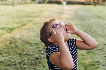 Cheerful emotional portrait of little girl with poor eyesight in eyeglasses outdoors in summer park