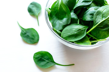 Fresh green spinach leaves in glass bowl on white table. Organic food, healthy diet, vegetarian food. Top view.