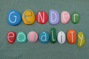 Gender Equality slogan composed with multi colored and carved stones over green sand