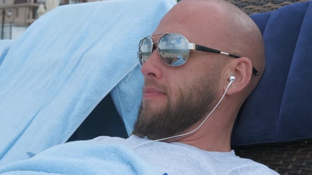 Man lies in headphones. The man on the beach lies in sunglasses.