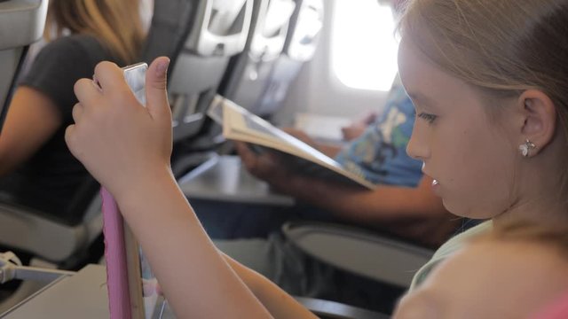 Adorable girl traveling by an airplane and using a digital tablet during the flight. Concept traveling abroad with kids.