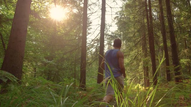 SLOW MOTION, CLOSE UP, LOW ANGLE, COPY SPACE, LENS FLARE: Unrecognizable fit man jumps over the camera while trail running through the idyllic sunlit forest in the summer. Athlete jogging in the woods