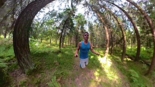SELFIE, WIDE ANGLE: Fit guy running through the scenic forest on a perfect summer day. Athletic man in tank top exploring the woods by going for a relaxing trail run. Man jogging through the wild.